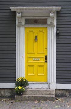 a bright yellow door sits in front of a gray house with white trim and columns