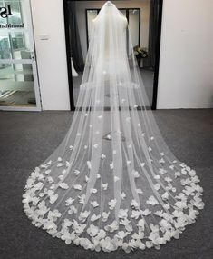 a wedding veil with white flowers on the bottom is shown in front of a doorway