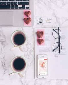 two cups of coffee next to an open book and cell phone on a marble table