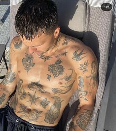 a shirtless man sitting in a chair with tattoos on his chest and arms, looking down