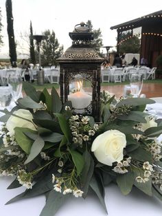 a lantern with flowers and greenery sits on a table