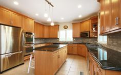 a kitchen with wooden cabinets and black counter tops, stainless steel appliances and an island in the middle