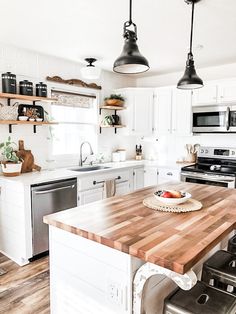 a kitchen with white cabinets and wooden counter tops, an island in the middle is surrounded by black appliances