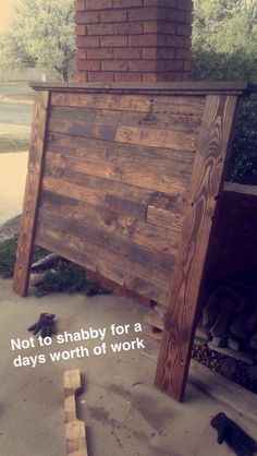 a wooden sign sitting on the ground next to a brick wall with words written below it