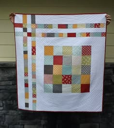 a person holding up a quilt made with squares