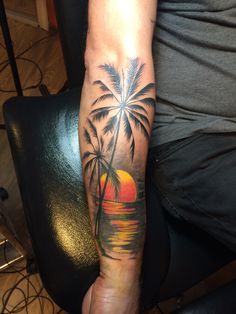 a man's arm with a palm tree and sunset tattoo on the left forearm