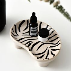 a white and black zebra print plate with two bottles on it next to a vase