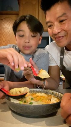 two men and a boy are eating food in a bowl together at the kitchen table