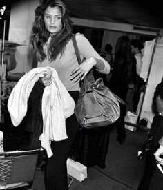 a black and white photo of a woman holding clothes in her hand while walking through an airport