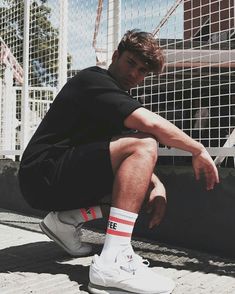 a man sitting on the ground with his legs crossed, wearing white sneakers and black t - shirt