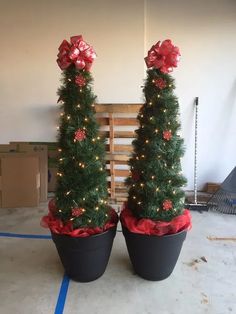 two potted christmas trees with bows and lights in the shape of cones on top