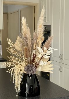 a black vase filled with dried flowers on top of a kitchen counter next to an oven