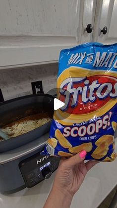 a hand holding a bag of chips in front of an air fryer