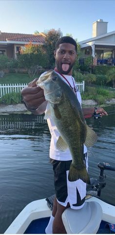 a man on a boat holding up a large bass he caught in the water while fishing