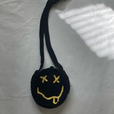 a crocheted smiley face bag hanging from a black string on a white wall