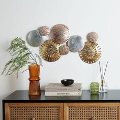 a wooden sideboard topped with lots of metal balls and plants next to a white wall