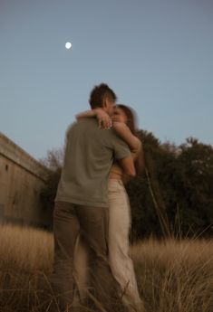 a man and woman embracing in the middle of a field at night with a full moon behind them