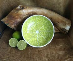 limes are sitting next to a piece of driftwood and a bowl on a chair