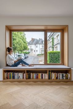 a woman sitting on top of a window sill next to a bookshelf