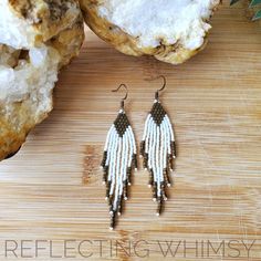 a pair of white and brown beaded earrings sitting on top of a wooden cutting board