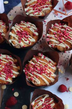 several muffins with white icing and raspberries in paper cups on a table