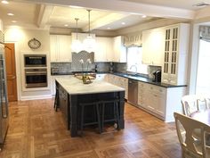 a large kitchen with an island in the middle and white cabinets on both sides, along with hardwood flooring