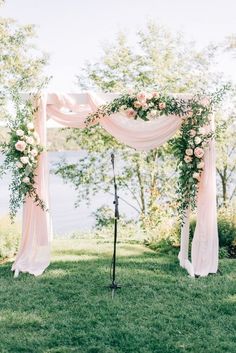 an outdoor wedding ceremony setup with pink drapes and flowers on the arch, near water