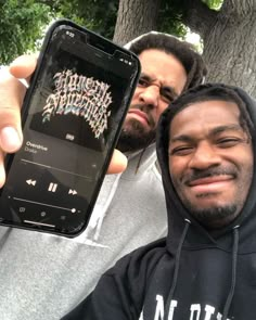 two men holding up their cell phones in front of them, one is smiling at the camera