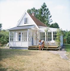 two people sitting on the porch of a small white house with an open front door