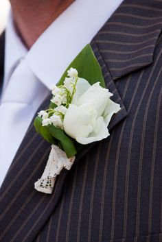 a boutonniere with white flowers and greenery attached to the lapel