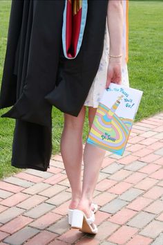 a person in a graduation gown is holding a book and standing on the brick path