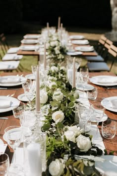 a long table is set with white flowers and candles for an elegant dinner party setting