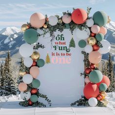 an arch decorated with balloons and garlands on top of a snow covered slope in the mountains