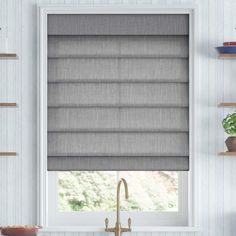 a kitchen window with roman shades in grey