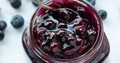 a jar filled with blueberries sitting on top of a white table next to berries