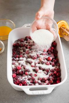 someone pouring sugar on top of cranberries in a white dish with oranges