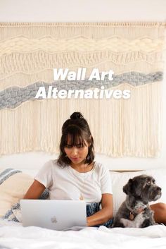 a woman is sitting on her bed while working on her laptop and dog sits next to her