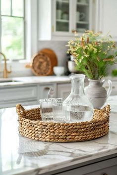 a glass pitcher and two glasses sitting on a counter in a kitchen with white cabinets