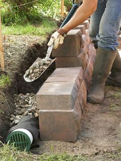 a woman is placing bricks into the ground to build a garden wall and planter