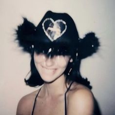 a woman wearing a black hat with a heart on the top and feathers around it