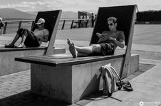 two people sitting on benches with their feet up and one person looking at his cell phone