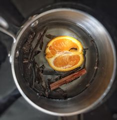 an orange is sitting in a pot with cinnamons