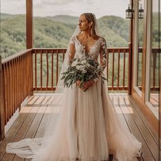 a woman in a wedding dress standing on a wooden porch with mountains in the background