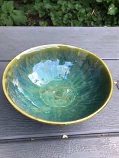 a green and yellow bowl sitting on top of a wooden table next to plants in the background