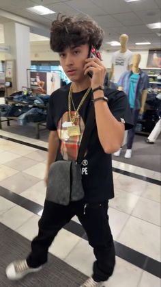 a young man is walking and talking on his cell phone while holding a purse in one hand