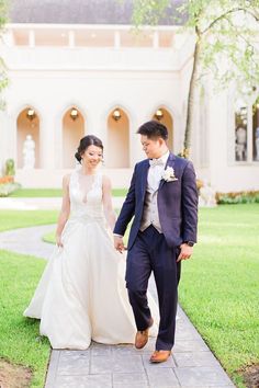 a bride and groom walking down a path in front of a large white building with arches