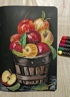 a painting of apples in a basket with crayons on the table next to it