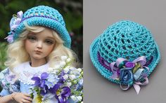 a doll wearing a blue crocheted hat with flowers on the brim and holding a bouquet of flowers