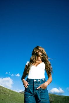 a young woman standing on top of a lush green field next to a blue sky