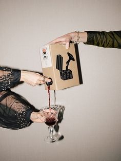 two women are pouring red wine into a glass with a cardboard box on the top